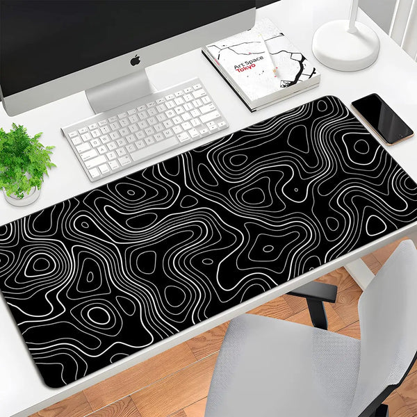 A black mouse pad with white contour lines is placed on a desk next to a computer and keyboard.