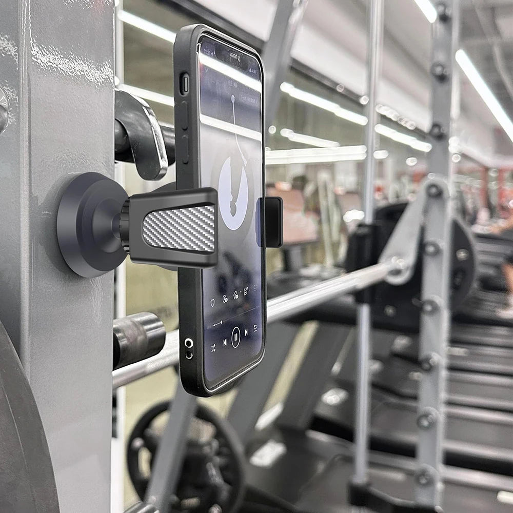 A black magnetic phone holder is mounted on a gym equipment frame, designed for fitness use.