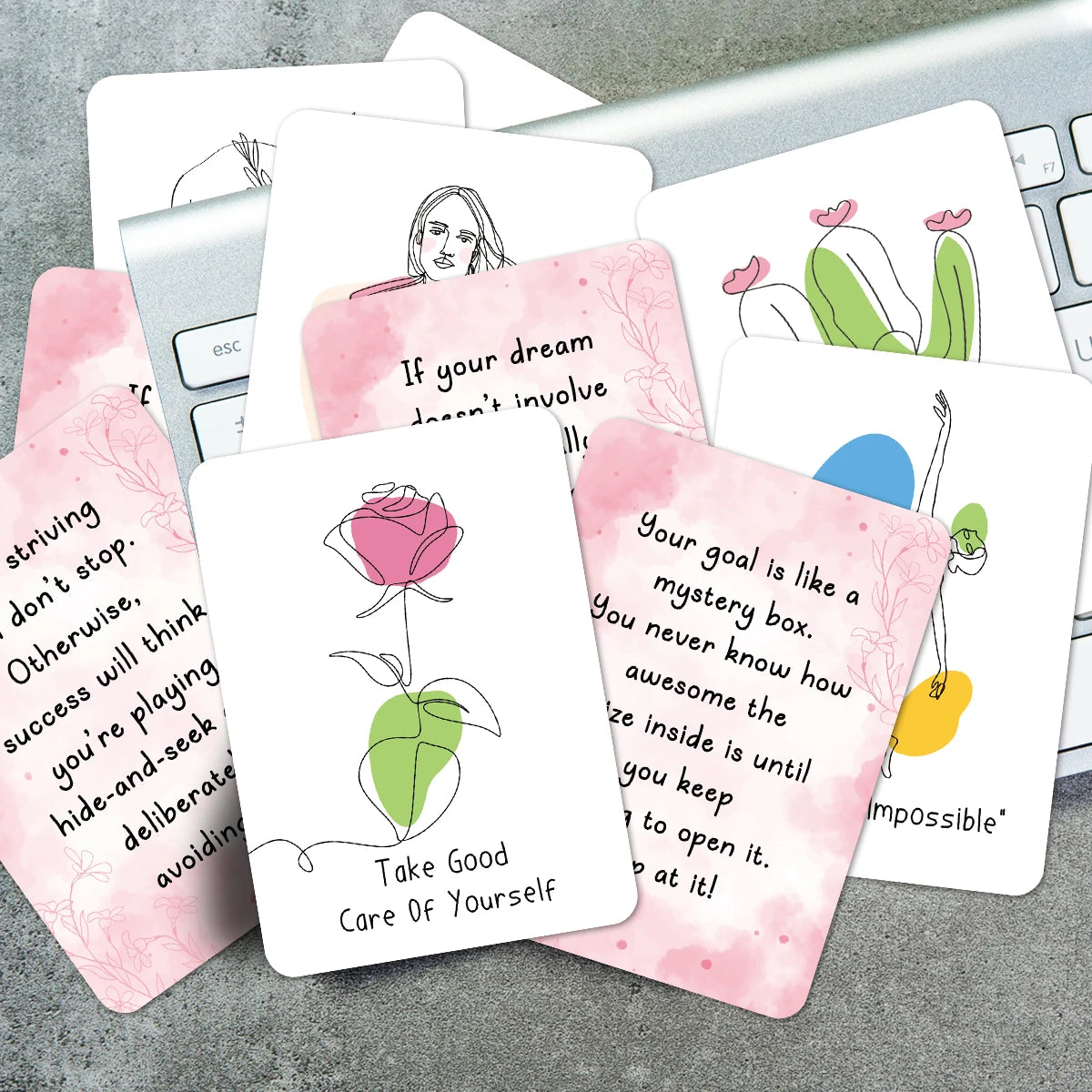A collection of pink and white affirmation cards featuring inspirational quotes and simple line drawings on a silver laptop.