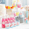 A display of pink and yellow adhesive stickers on wooden skewers arranged in various glass jars and on a white platter.