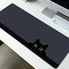 A black cat silhouette mouse pad is placed on a white desk mat next to a silver electronic device.
