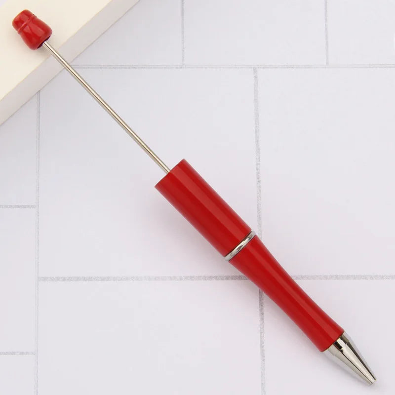 A red DIY beadable pen with a silver tip and a red cap resting on a white surface.