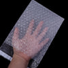 Eine Hand drückt eine klare, selbstversiegelnde Schaumverpackung auf eine dunkle Oberfläche.