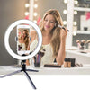 A woman uses an LED ring light with a tripod stand to film herself for makeup or streaming.