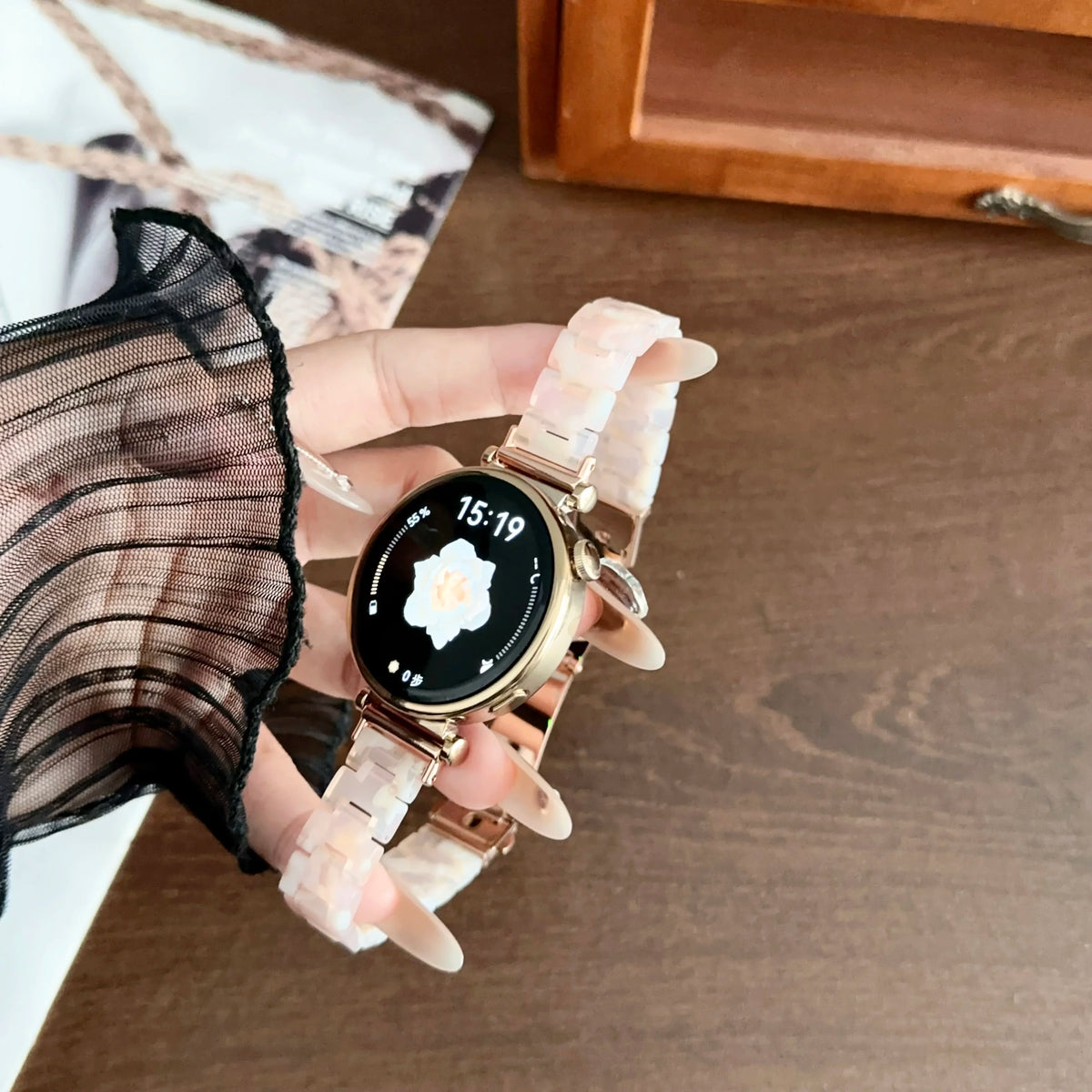 A hand is holding a resin beaded watch with a light pink band and a black face displaying the time 15:19.