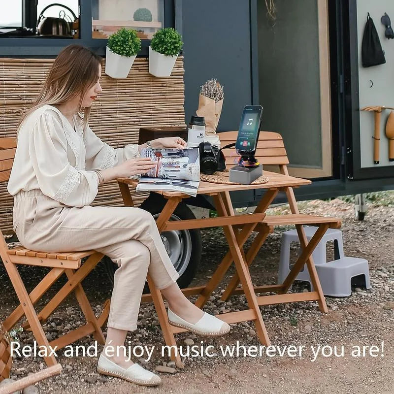 A woman sits on a wooden chair outdoors relaxing while using a wireless speaker with an adjustable phone stand and night ligh