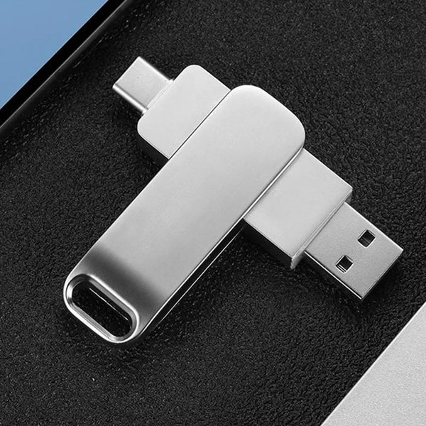 Clé USB argentée avec adaptateur OTG posée sur une surface noire.