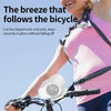 A woman is using a portable clip-on fan attached to a bicycle, demonstrating its secure fit.