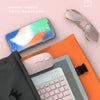 A light volume Bluetooth keyboard and mouse combo is shown next to a smartphone and a folder on a pink background.
