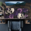 A dark desk mat featuring a gothic design of skulls and purple roses placed on a wooden desk.