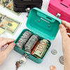 A teal steel cash box with a hinged lid is open, revealing stacks of coins and a banknote next to some paper currency.