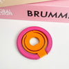 A pink magnetic phone grip and stand with an orange foldable ring resting on a white surface.