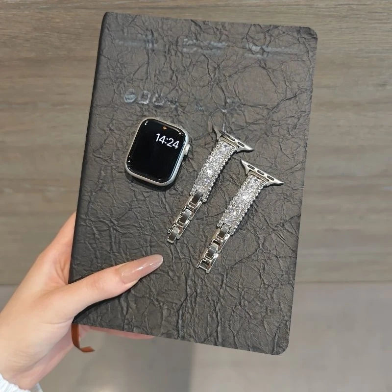 A close-up of a black leather-bound item showing a smartwatch and two crystal-embellished watch straps.