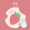 A round pink mouse pad featuring a strawberry pattern and Japanese text on a white computer mouse.