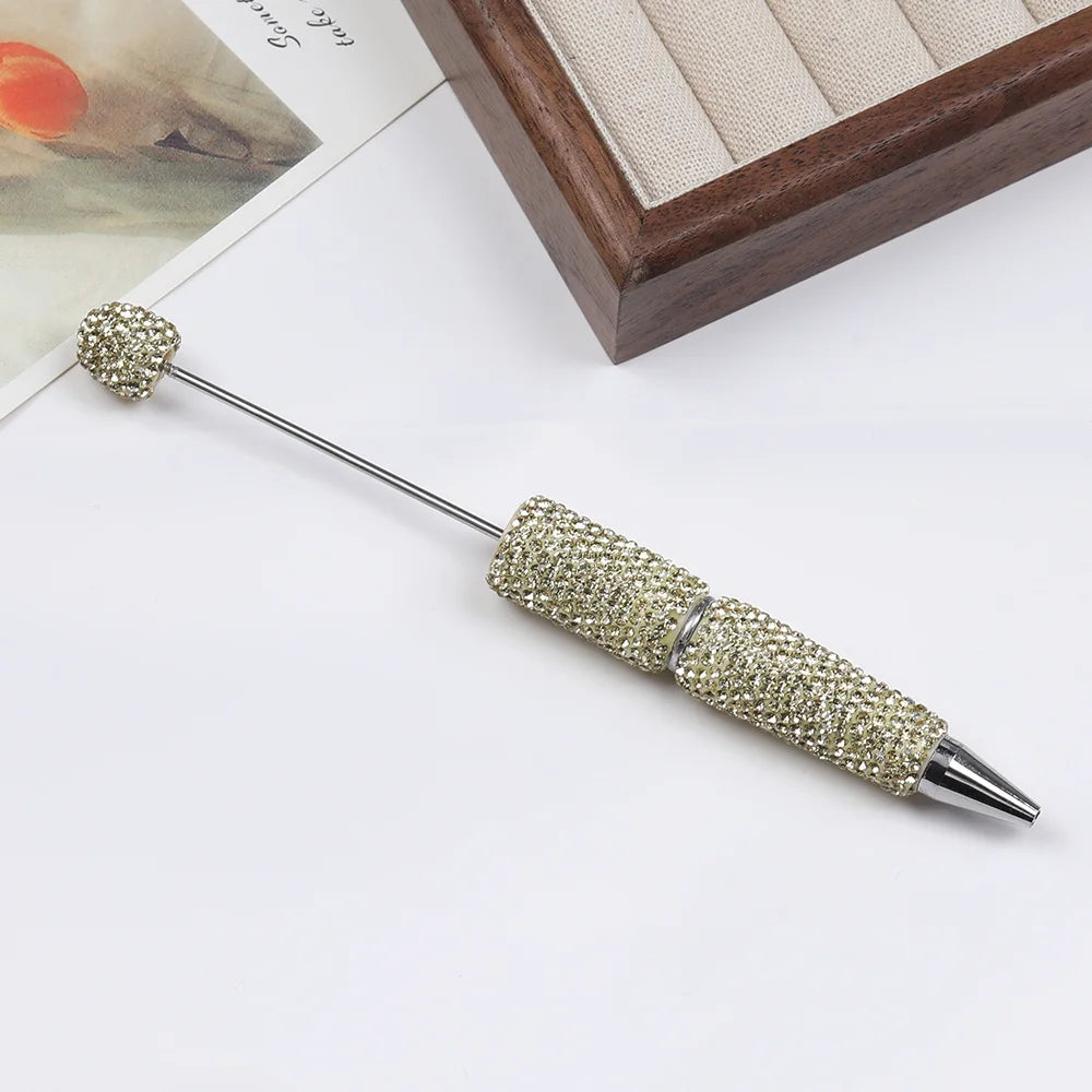A silver pen with a rhinestone-encrusted tip and a decorative gold-colored ball on the end.