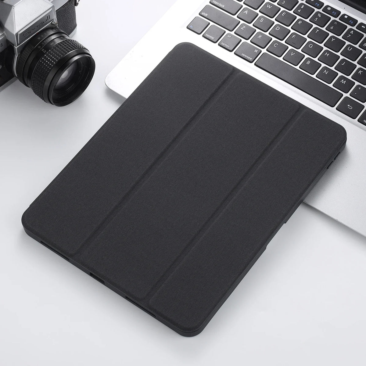 A black retro marbling skin for an iPad Pro placed next to a silver camera and a white laptop keyboard.
