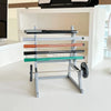 A gray barbell rack organizer with multiple colored bars for holding pens or tools on a white desk.