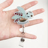 A hand holds a sparkly badge reel featuring a cute, speckled turtle nurse design.