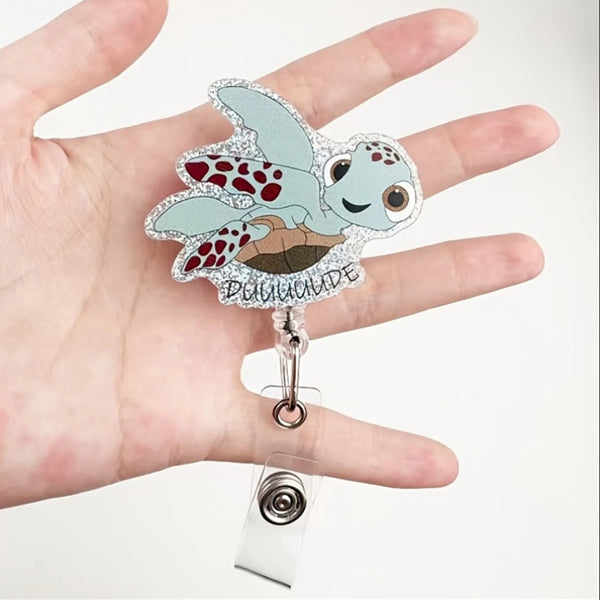 Eine Hand hält einen funkelnden Badge-Reel mit einem niedlichen, gesprenkelten Schildkröten-Krankenschwester-Design.