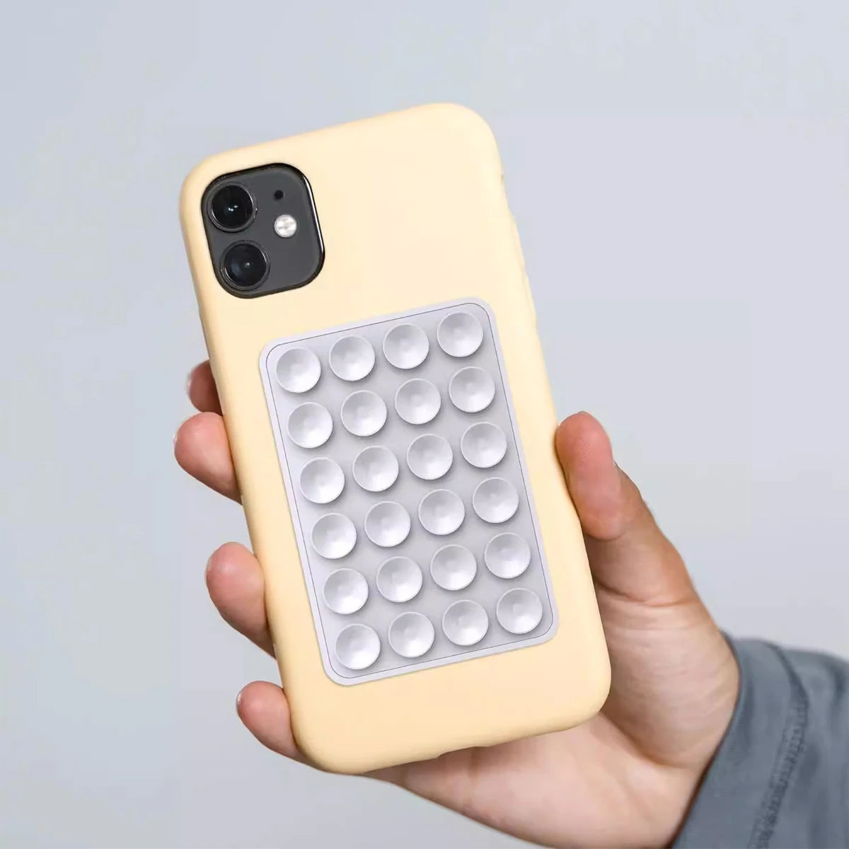 Una mano sostiene un smartphone amarillo con un soporte de ventosa de silicona transparente unido a la parte posterior.