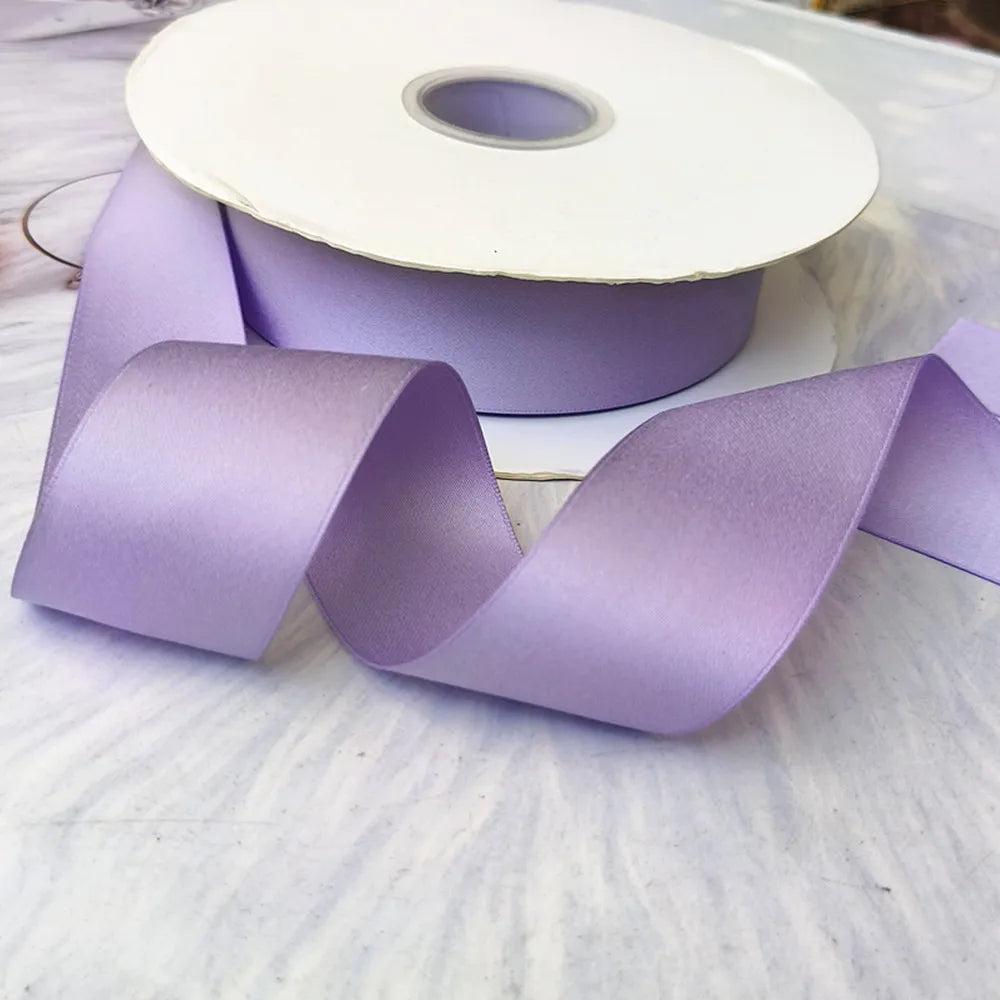 Roll of matte finish satin ribbon in light purple color lying on a white surface.