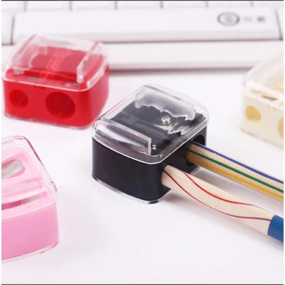 Afilador automático negro de doble orificio con un lápiz de madera insertado, junto a otros afiladores de plástico.