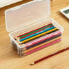 A clear storage box with a lid contains various colored pencils and other craft supplies on a wooden surface.