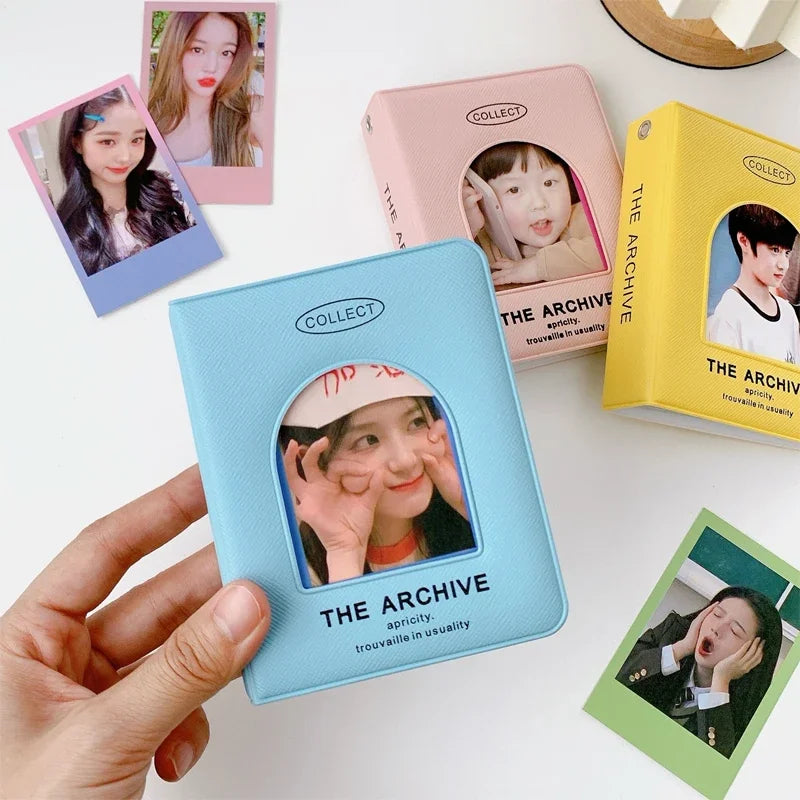 A hand holds a light blue hollow photo card binder labeled The Archive for Kpop albums, surrounded by similar pink and yellow