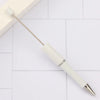 A white DIY beadable pen is shown lying on a white tiled surface.