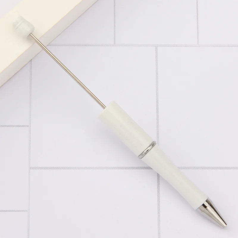 A white DIY beadable pen is shown lying on a white tiled surface.