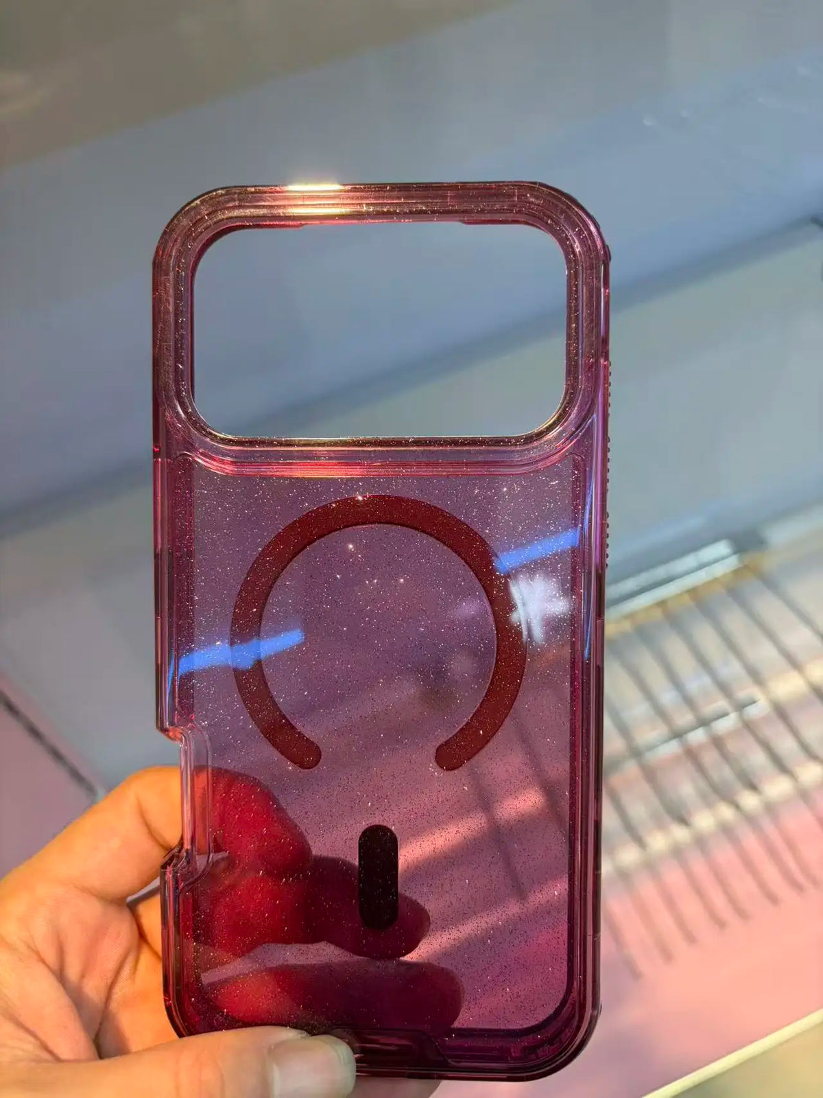A hand holds a clear pink glitter shockproof magnetic case for an iPhone.