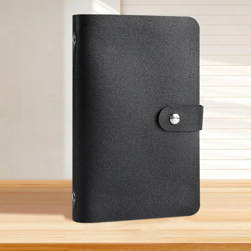 A black reusable envelope money saving challenge binder with a silver clasp on a wooden surface.