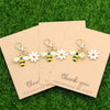 A set of five cute ladybug and daisy keychains displayed on pink kraft paper against a green background.
