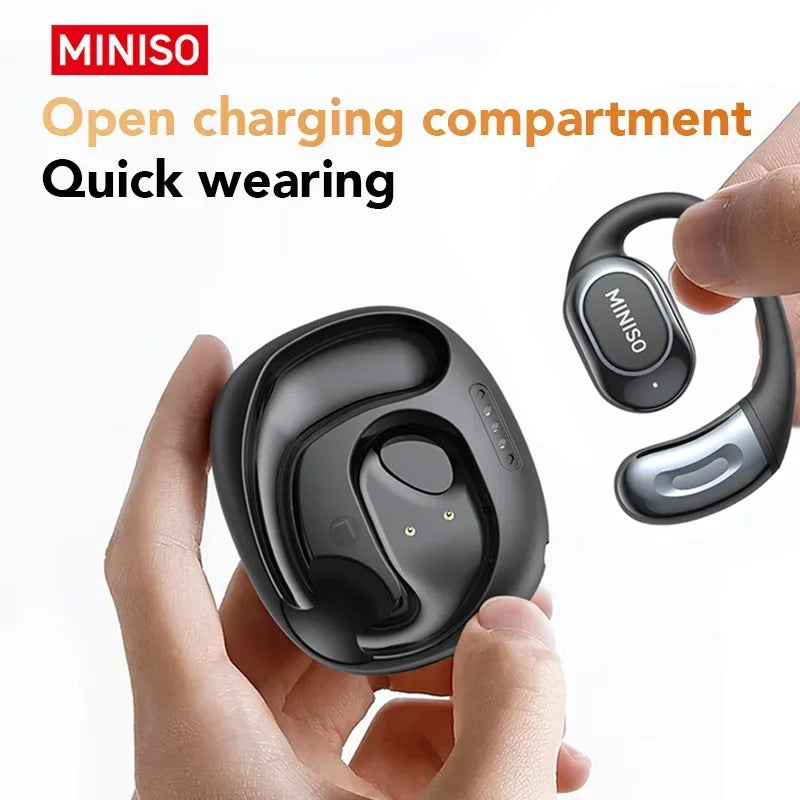 A hand holds a black open charging compartment sports earbud with a silver charging case nearby.