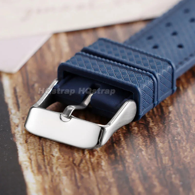 A close-up of a dark blue perforated silicone watch strap with a silver quick release buckle resting on a wooden surface.