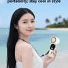 A woman holds a portable rechargeable handheld cooling fan with a lanyard, against a tropical beach background.
