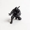 A matte black ninja figurine holding a pen, shown from above.