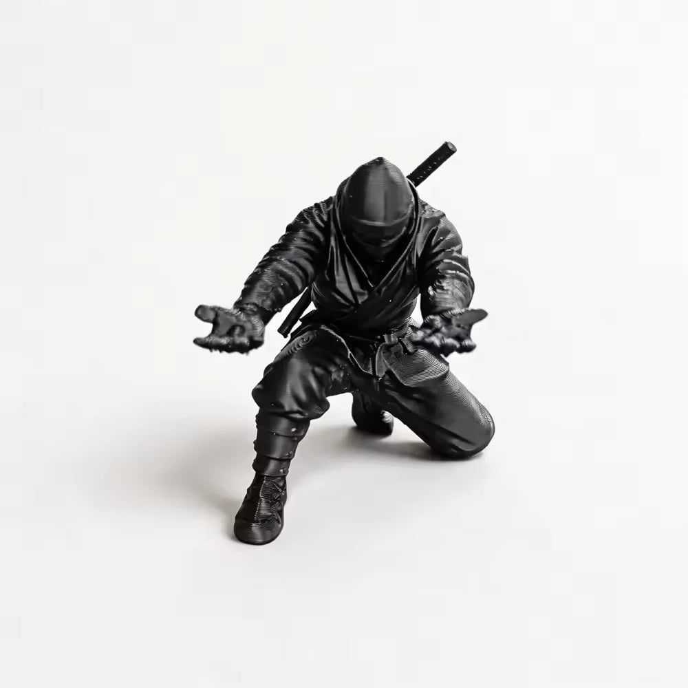 A matte black ninja figurine holding a pen, shown from above.