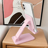 A pink adjustable desktop phone stand holding a smartphone in a vertical position on a wooden table.
