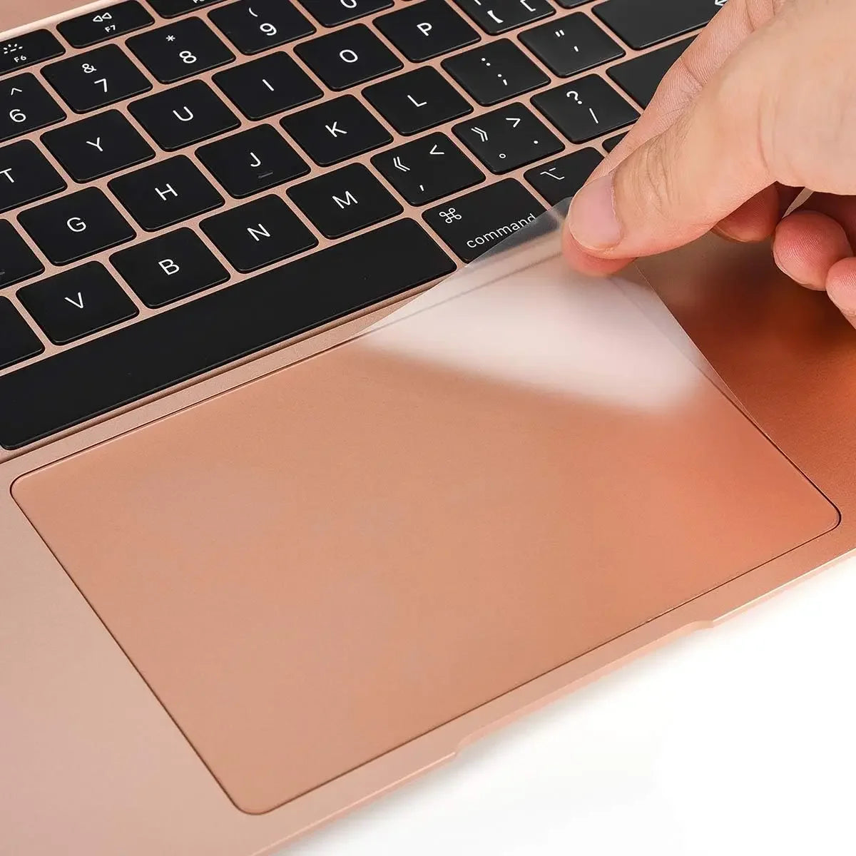 A hand is interacting with a rose gold laptop, showing the keyboard and a protective trackpad cover.