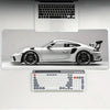A white sports car is displayed on a gaming mousepad with a laptop and keyboard in the background.