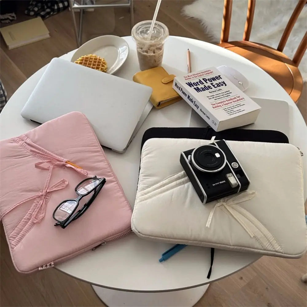 A white laptop sleeve case is shown on a table with various accessories like glasses and a notebook.