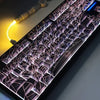 A close-up view of a mechanical keyboard with translucent keycaps featuring a spiderweb design and glowing purple lighting.