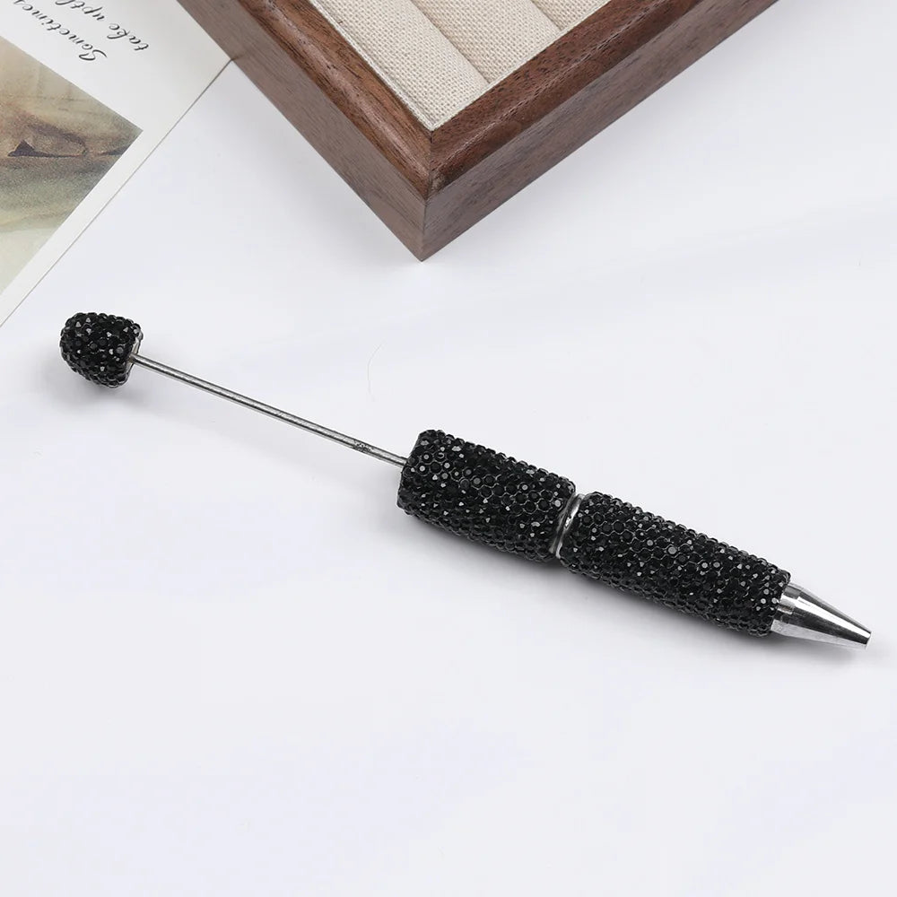 A black beaded pen accessory with a silver tip is shown on a white background.