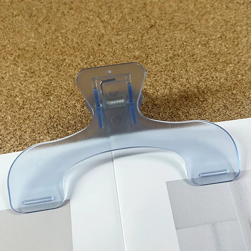 Clear plastic book page clips with a curved shape resting on a brown textured surface.