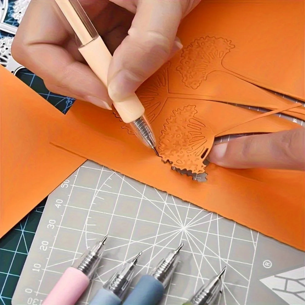 A hand uses a craft knife pen to cut an orange paper template on a grid surface.