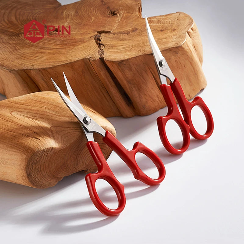 A pair of red stainless steel embroidery scissors resting on a wooden surface.