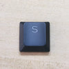 A close-up view of a dark blue mechanical keyboard keycap labeled with the letter S