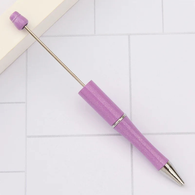 A purple DIY beadable pen with a silver band and a pointed tip resting on a white surface.
