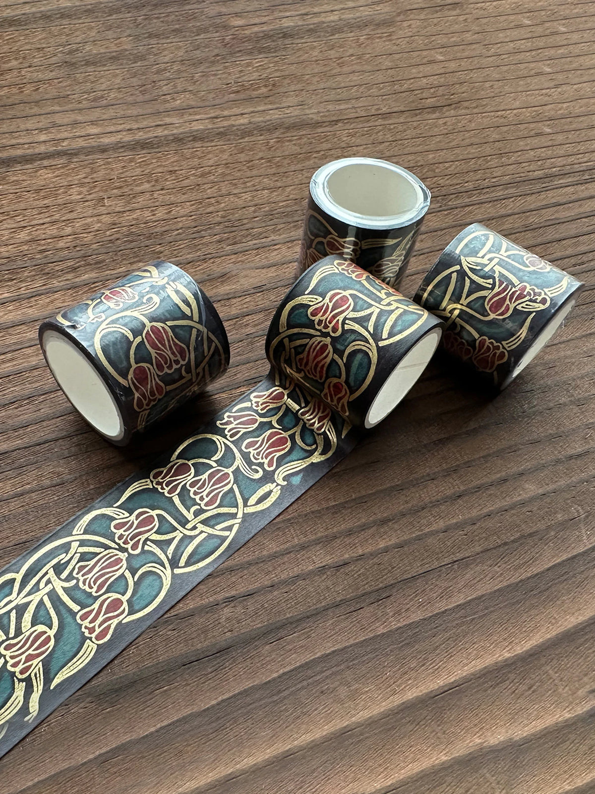 A set of metallic gold washi tape rolls featuring floral patterns laid out on a wooden surface.